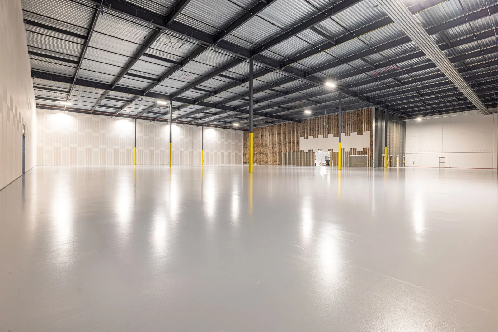 Inside a new steel warehouse near completion, with steel joists and metal roof deck overhead.