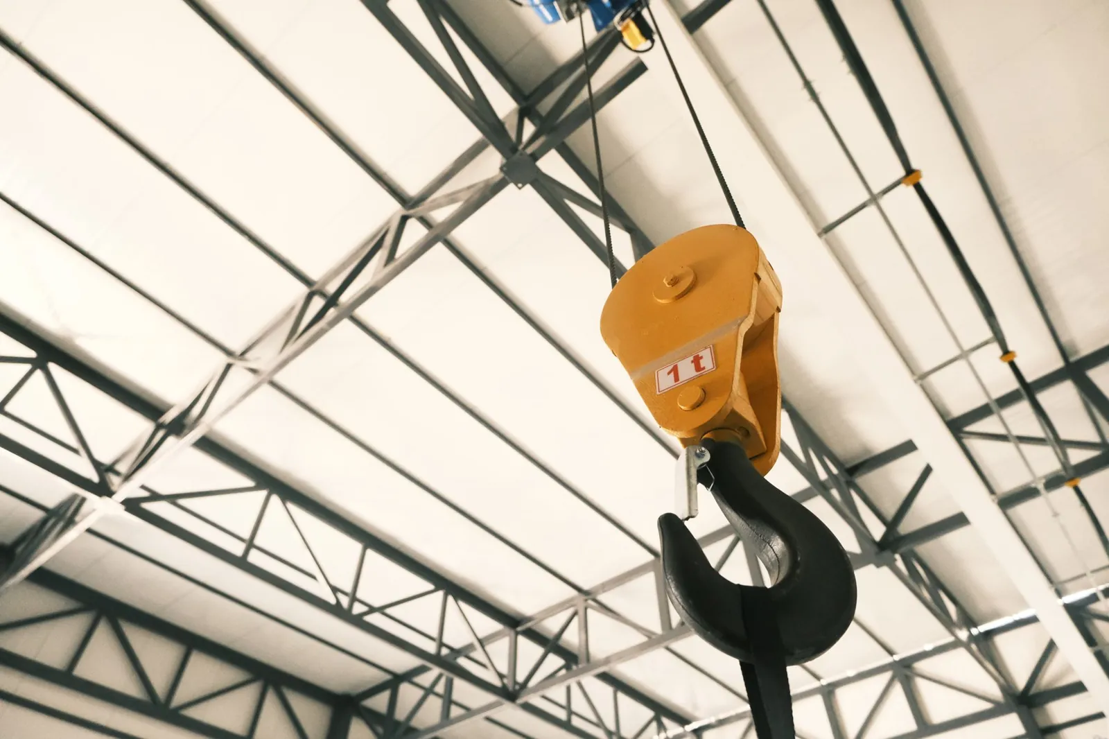 Crane hook hanging under the steel roof framing of a new industrial building.